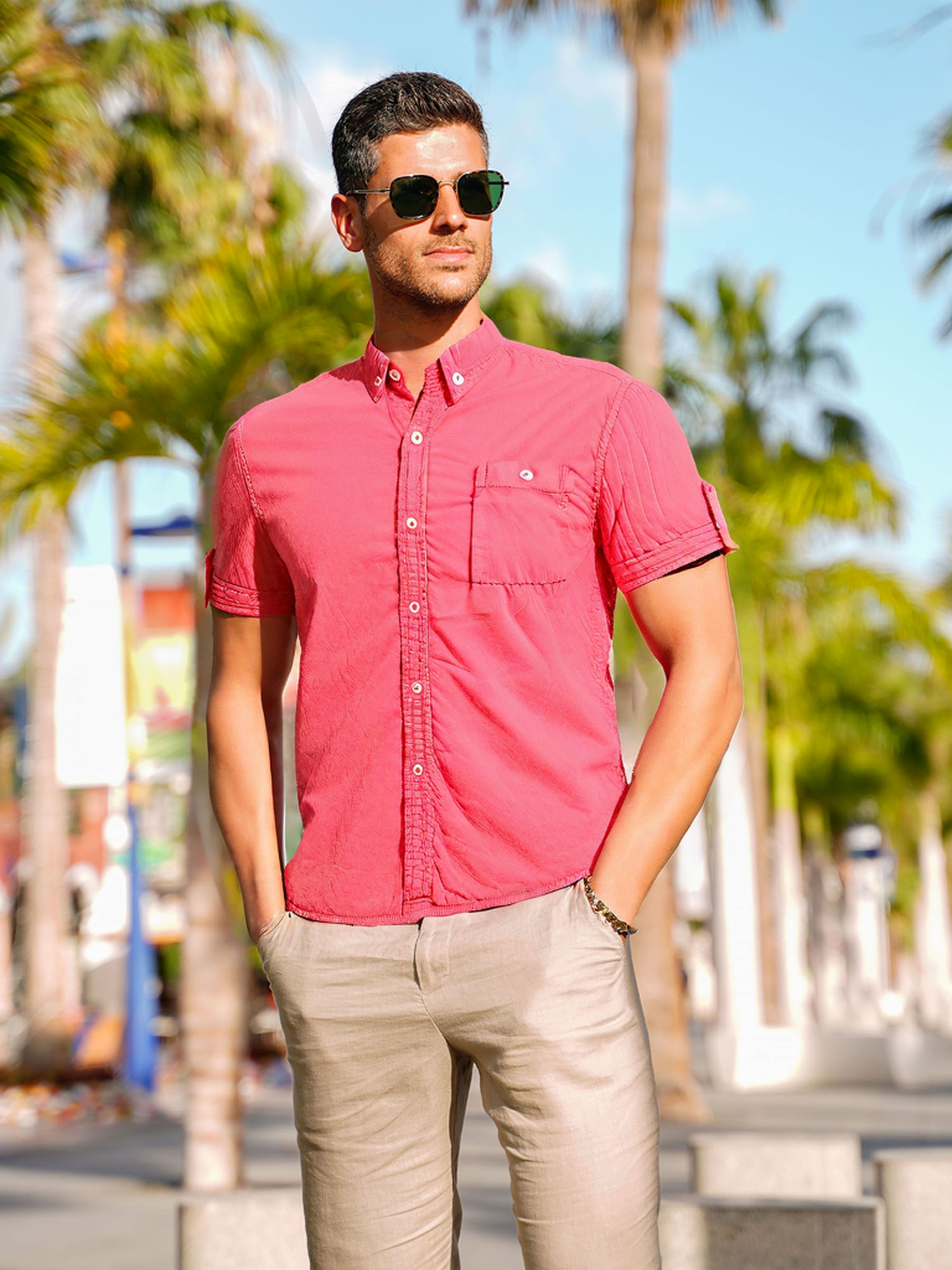 Un uomo che indossa occhiali da sole, guarda a sinistra, indossa una camicia abbottonata rosa-rossa.